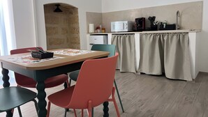 Une cuisine compacte équipée d’un four à micro-ondes, d’une machine à café et d’un petit réfrigérateur. On y trouve une table à manger avec des chaises et un joli tapis décoratif.