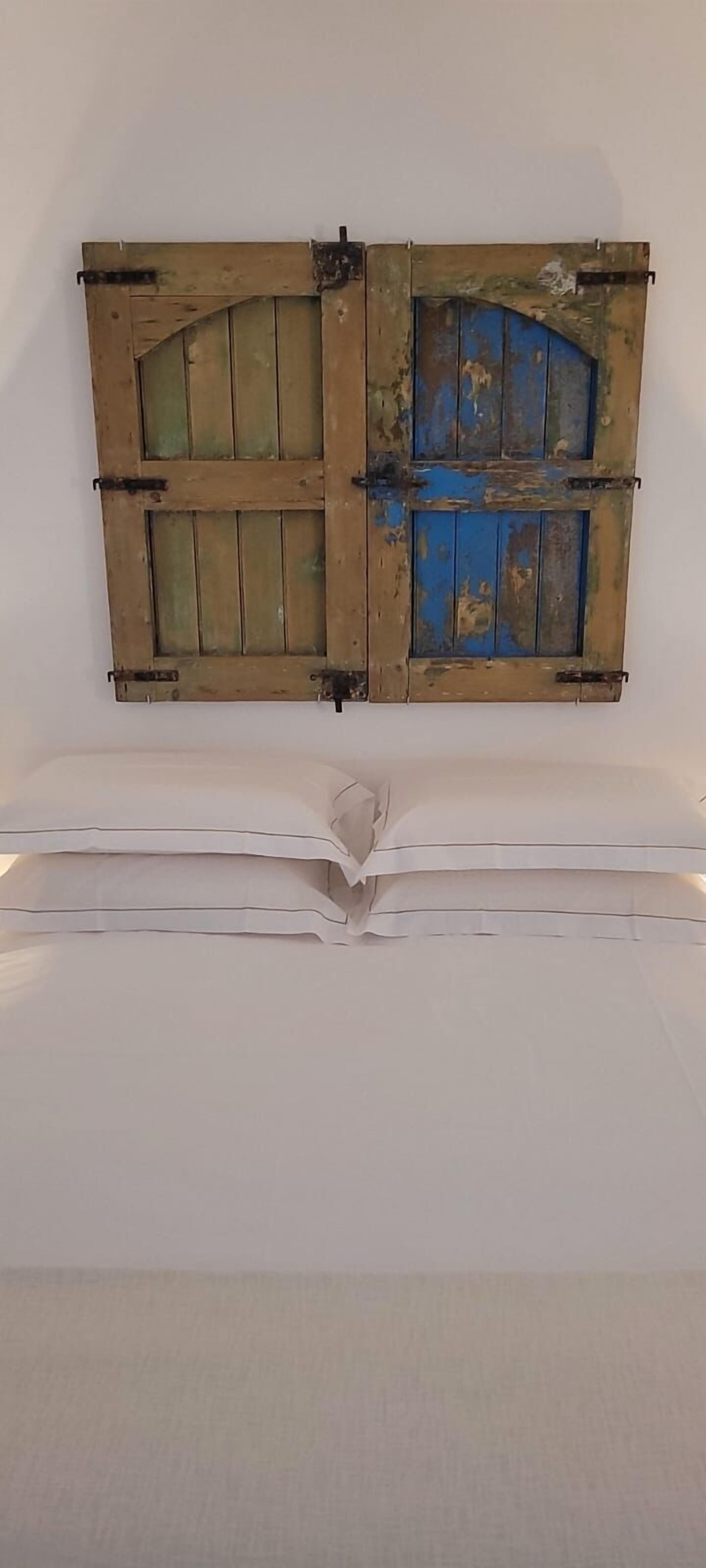 A room with a white bed and a rustic wooden door with a blue panel.
