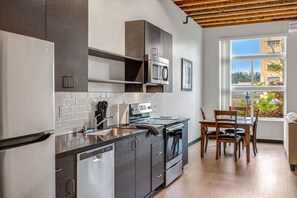 A modern kitchen with stainless steel appliances, a dining area with wooden chairs, and a view of a building outside.