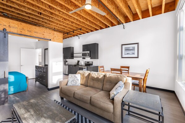 A modern living space with a wooden ceiling, a sofa, a dining table, and a kitchen area.
