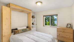 Un dormitorio con cama, cabecera de madera, cómoda, ventana con vistas y estanterías empotradas.