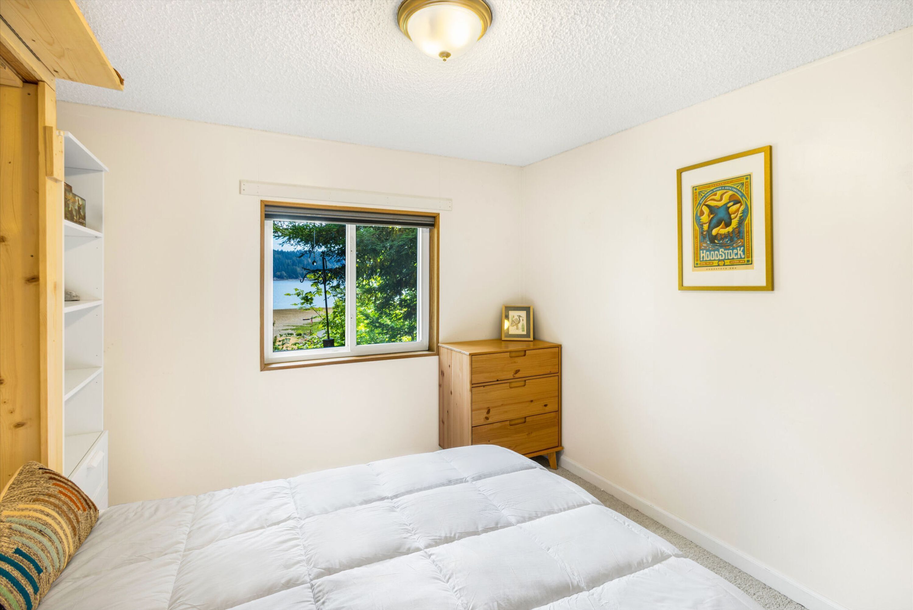 A bedroom with a bed, a wooden dresser, a window with a view, and a framed picture on the wall.