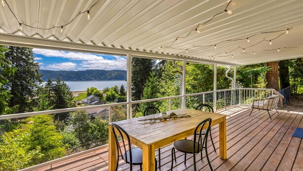 Una terraza de madera con una mesa y sillas, con vista a un lago y una zona boscosa.