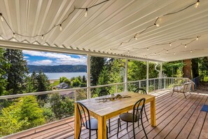 A wooden deck with a table and chairs, overlooking a lake and forested area. - Canal Cliff Cottage in Belfair (Belfair)