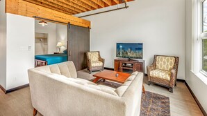 A spacious living room with a high ceiling, wooden beams, a large window, a sofa, two armchairs, a coffee table, and a flat-screen TV. - Tracyton Condo 202 in Bremerton (Bremerton)