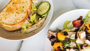 Deux assiettes de salade composées de divers légumes et fruits, dont l’une est accompagnée d’une tranche de pain grillé.