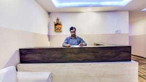 Un comptoir d’accueil avec une personne assise derrière, une lampe fixée au mur et un petit espace salon situé devant.