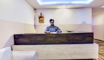 Un mostrador de recepción con una persona sentada detrás, una lámpara de pared y un pequeño espacio de asientos al frente.