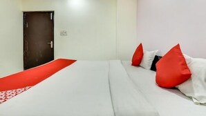 A hotel room with a bed, a red runner, and red and white pillows.