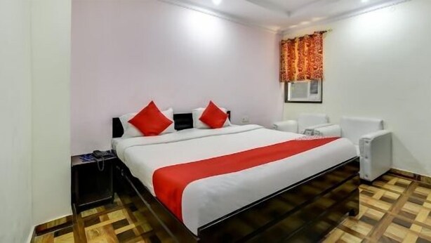 A hotel room with a large bed, a bedside table, a chair, and a window with curtains.