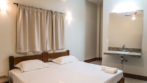 Camera d'albergo con un letto, una testiera in legno, un bagno con lavandino e specchio, e tende color beige.