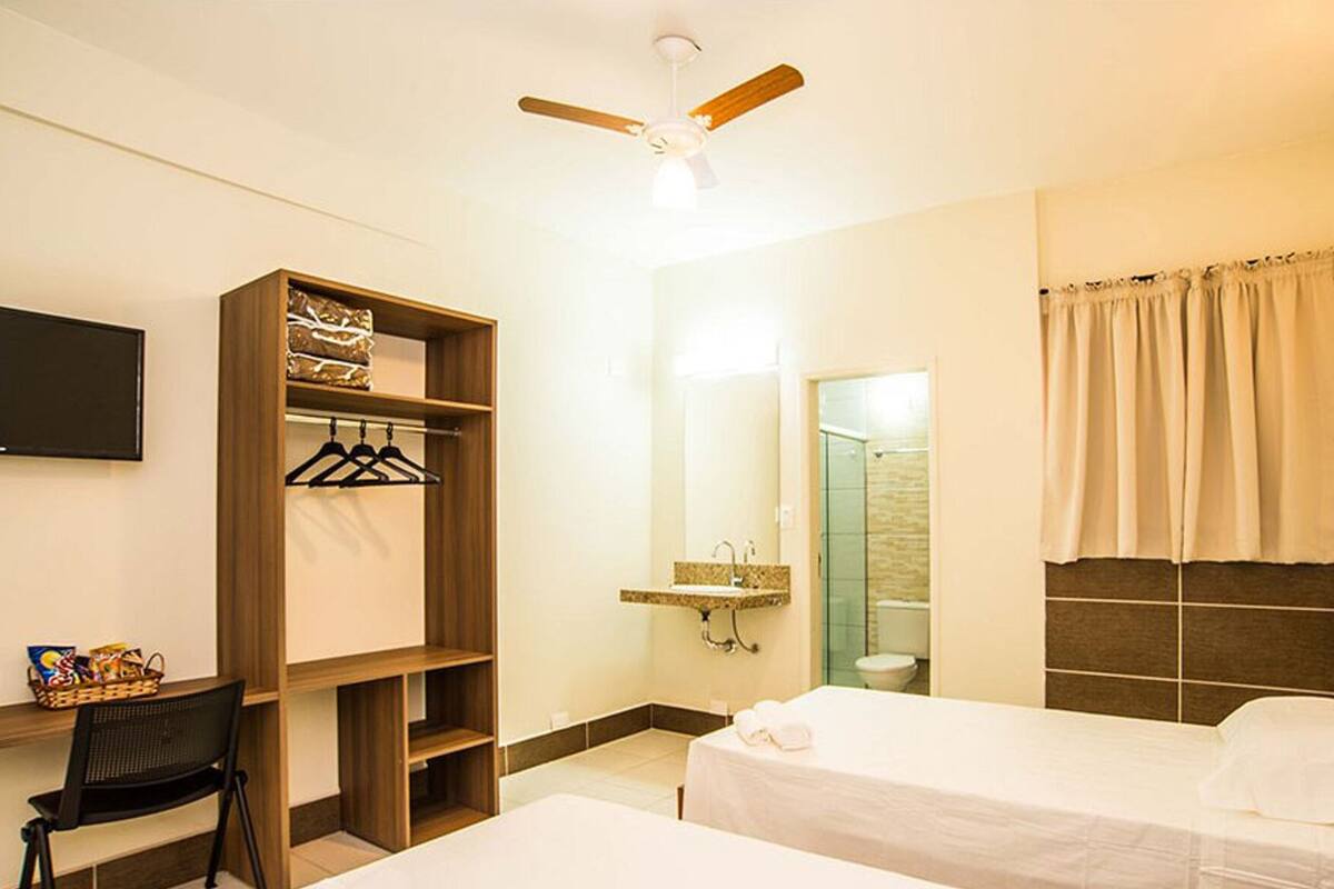 A hotel room with two beds, a wardrobe, a desk with a chair, a television, and a shower area.