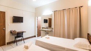 Camera d'albergo con un letto, una scrivania con una sedia, una televisione, un bagno con un lavandino e uno specchio, e una tenda.