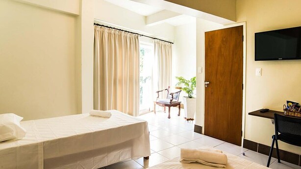 Camera d'albergo con un letto, una scrivania, una sedia, una televisione e una porta che dà su un balcone.