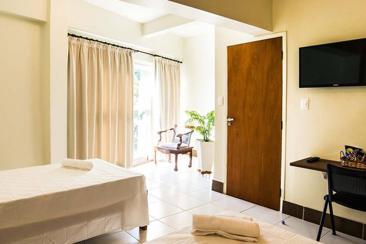 A hotel room with a bed, a desk, a chair, a television, and a door leading to a balcony.