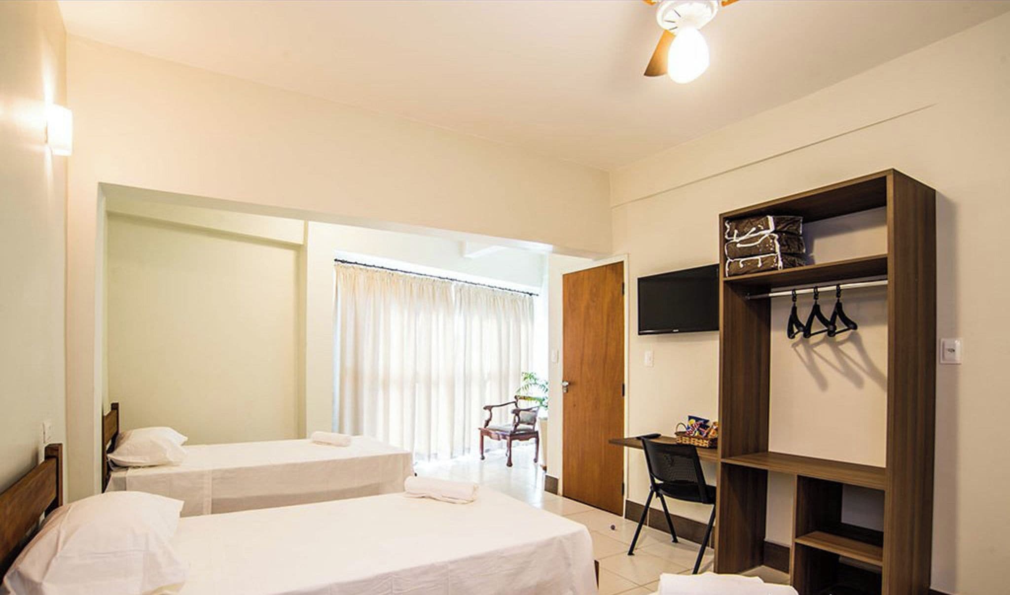 A hotel room with two beds, a desk, a chair, a TV, and a wardrobe.