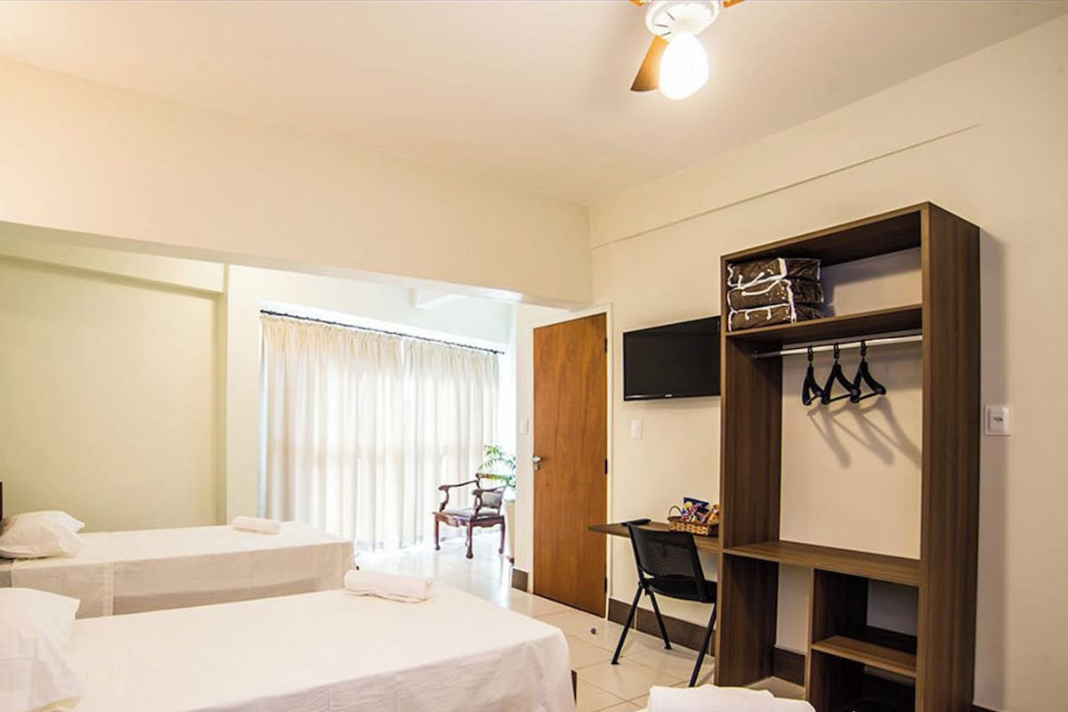 A hotel room with two beds, a desk, a chair, a TV, and a wardrobe.