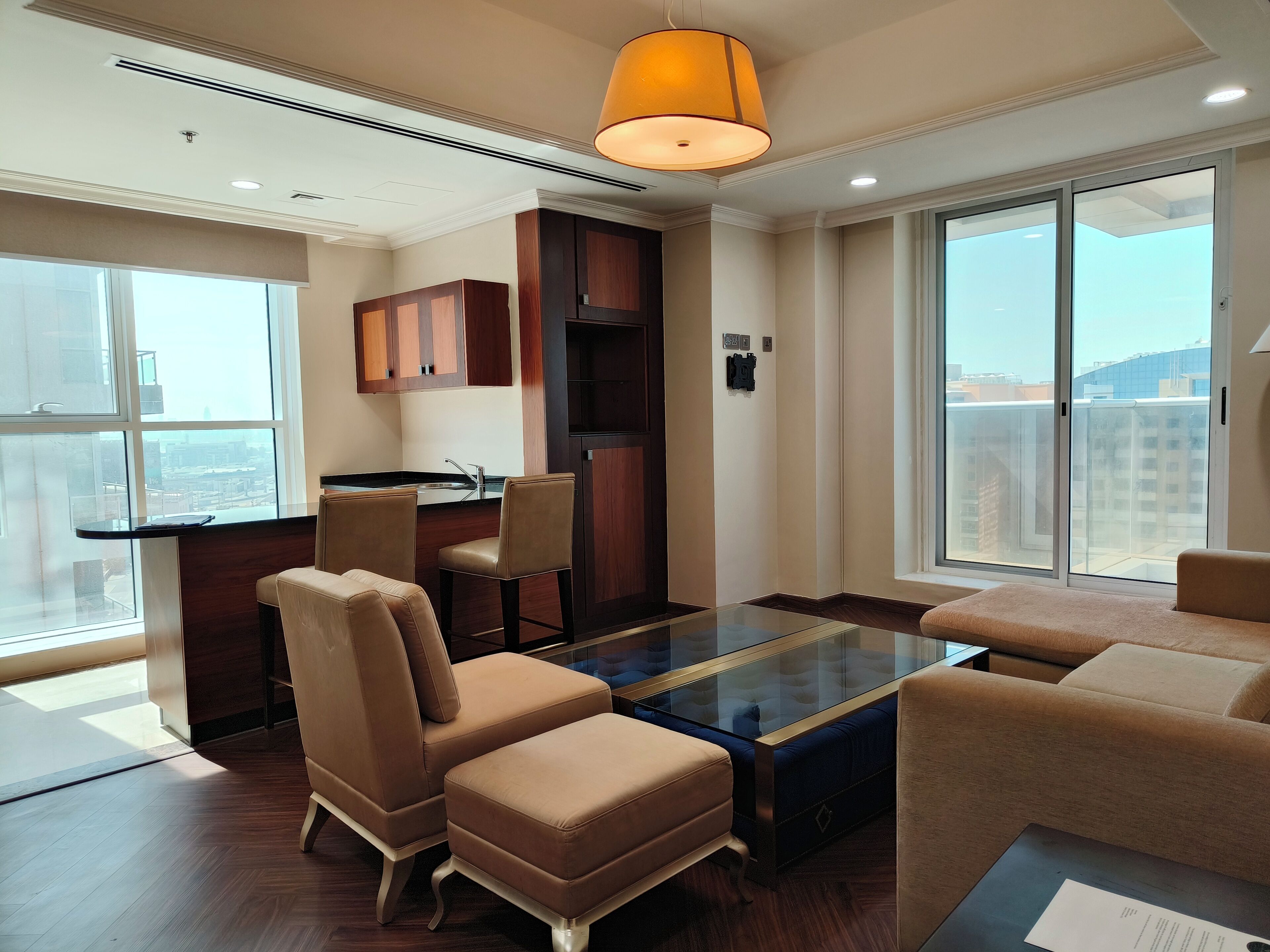 A modern living room with a glass coffee table, leather sofas, and a kitchen area with wooden cabinets.
