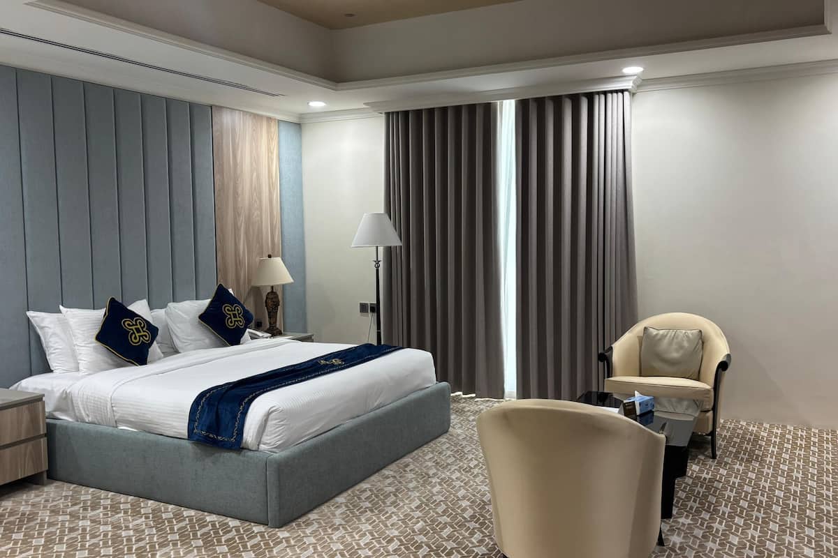 A hotel room with a large bed, a desk, a chair, and a window with curtains.
