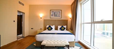 A hotel room with a large bed, a bench, a view of the city, and a painting on the wall.