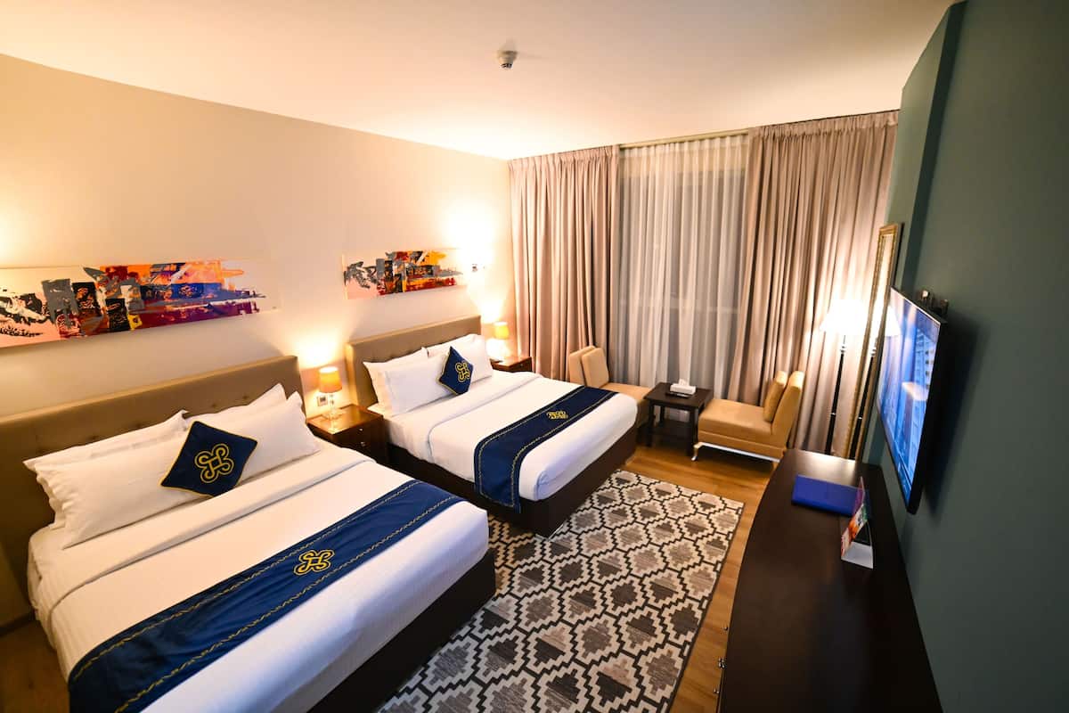 A hotel room with two beds, a TV, a desk, a chair, and a patterned rug.