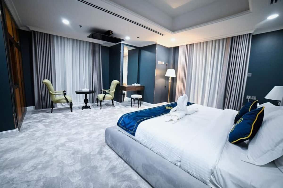 A hotel room with a large bed, two armchairs, a small table, a desk, and a lamp.