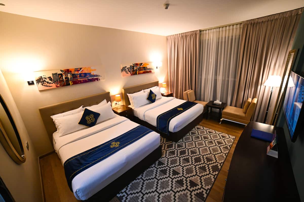A hotel room with two beds, a sofa, a TV, and a patterned rug.
