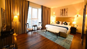 A hotel room with a large bed, two bedside tables with lamps, a chair, a small table, and a window with curtains. - Seven Seas Hotel  (Dubai)