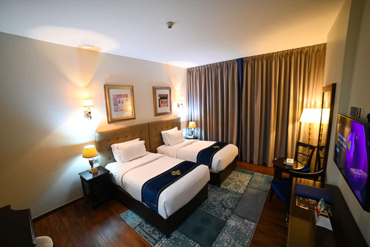 A hotel room with two beds, a TV, a desk, and a chair.