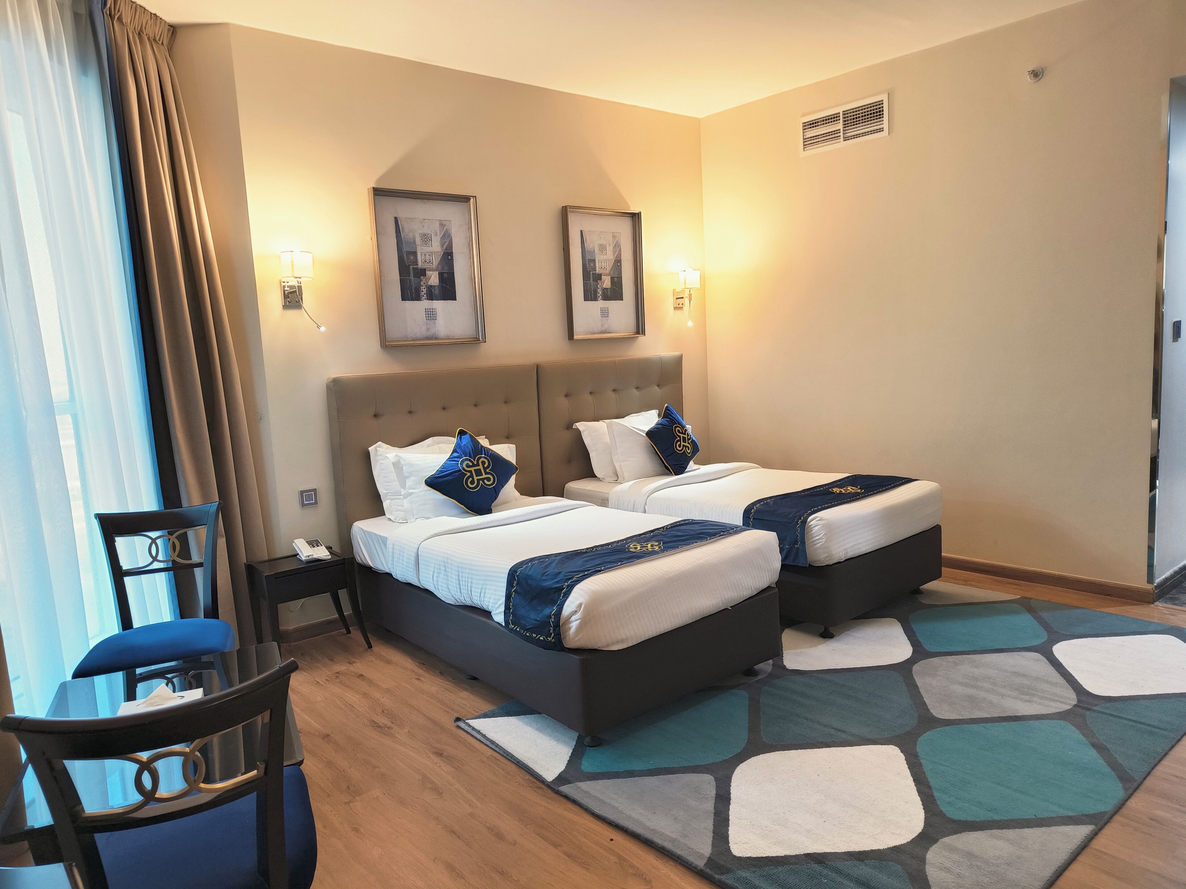 A hotel room with two beds, a chair, a desk, and a patterned rug.