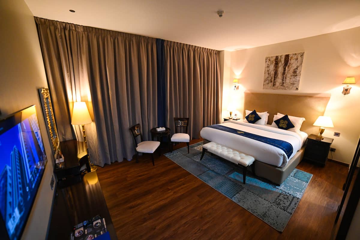 A hotel room with a large bed, two bedside tables, a TV, a desk, and a chair.