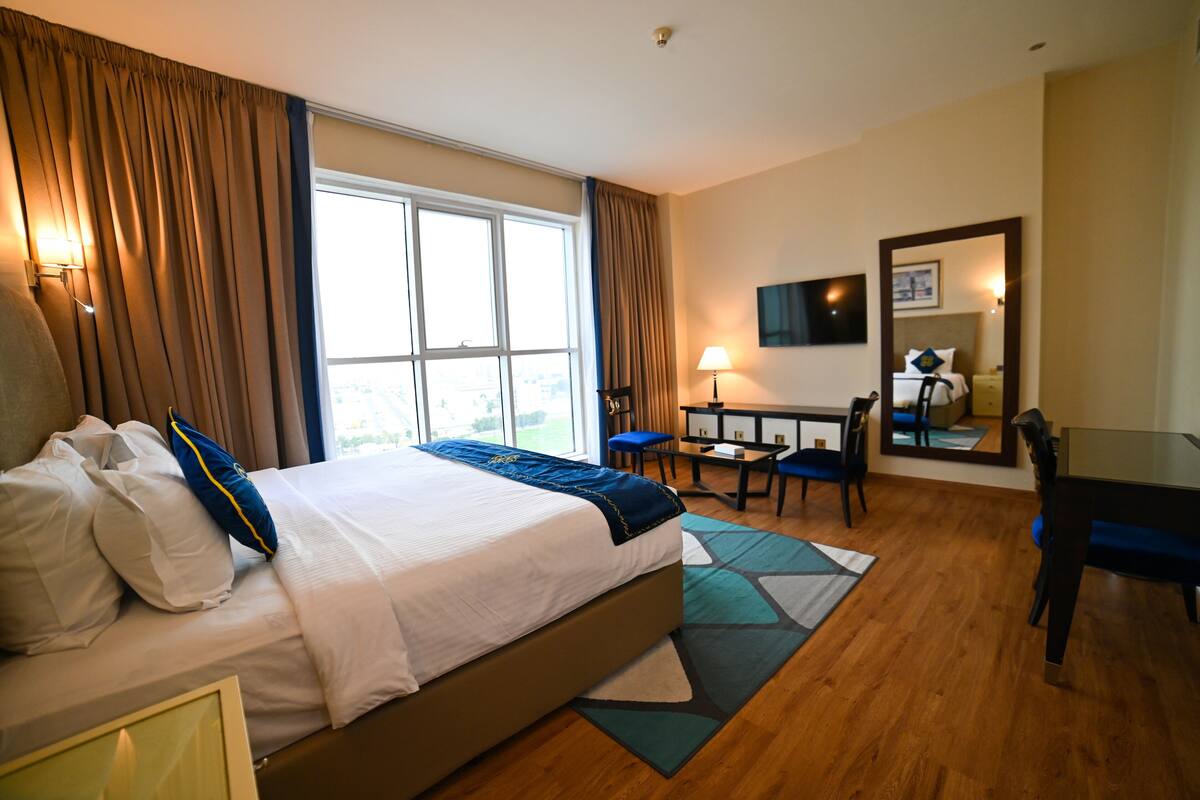 A hotel room with a large bed, a desk, a chair, a TV, and a window with curtains.