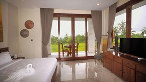 A hotel room with a bed, a TV, a wooden cabinet, and a balcony with a view of palm trees.
