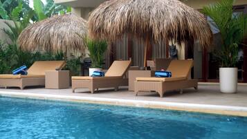 Relax by the pool with lounge chairs and thatched umbrellas providing shade.