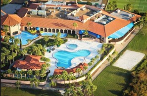 An aerial view of a resort with multiple swimming pools, palm trees, and a tennis court.