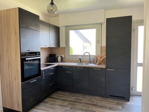 A modern kitchen with dark cabinetry, a built-in oven, a coffee maker, and a window providing natural light.