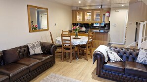 A living room with two brown leather sofas, a dining table with chairs, wooden cabinets, and a mirror on the wall. - Lake’s End Lodge.  (South Cerney)