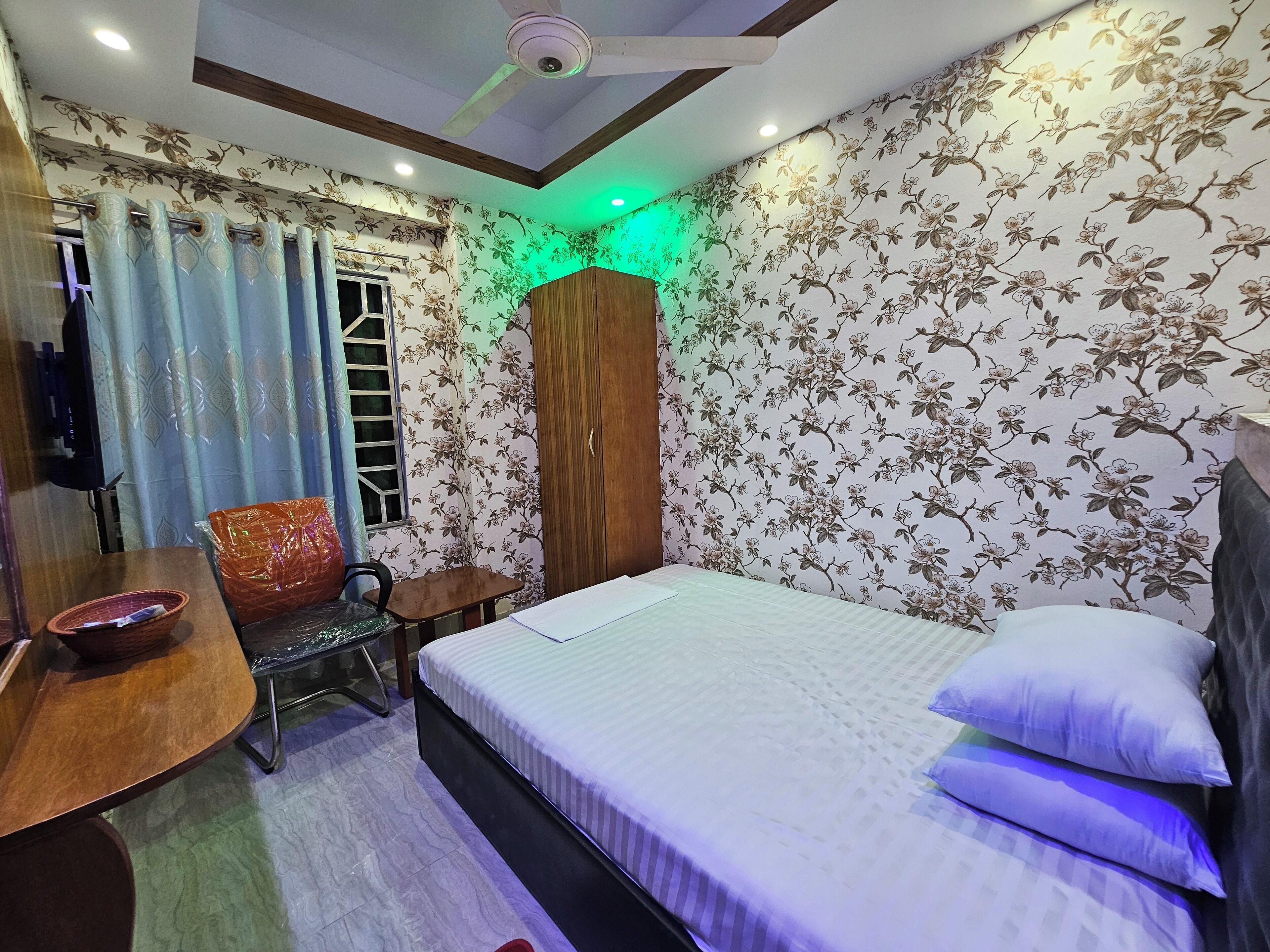 A bedroom with a bed, a desk, a chair, a wardrobe, and a window with curtains.