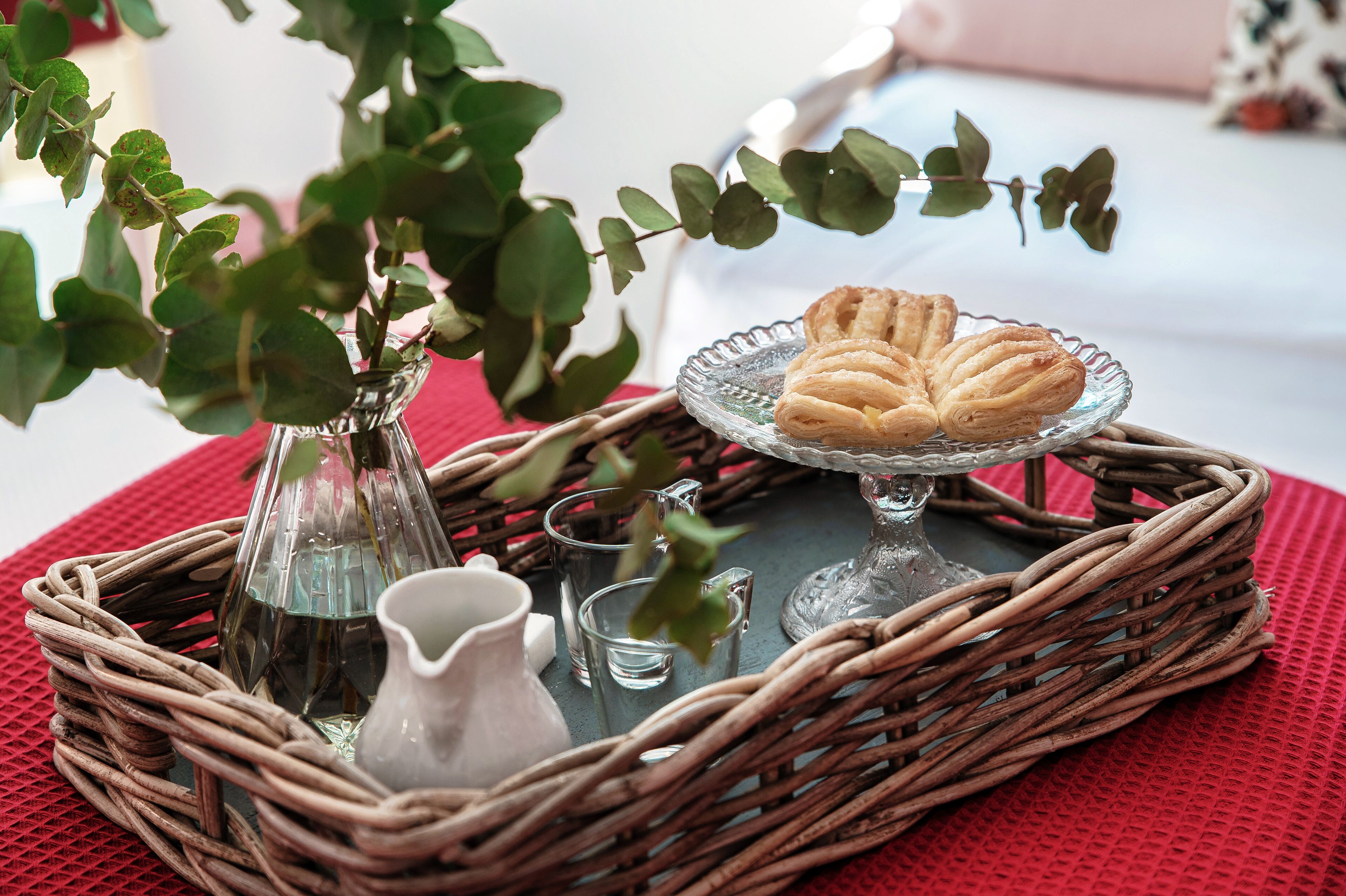 A wicker tray with a glass vase, a pitcher, and a plate of pastries.