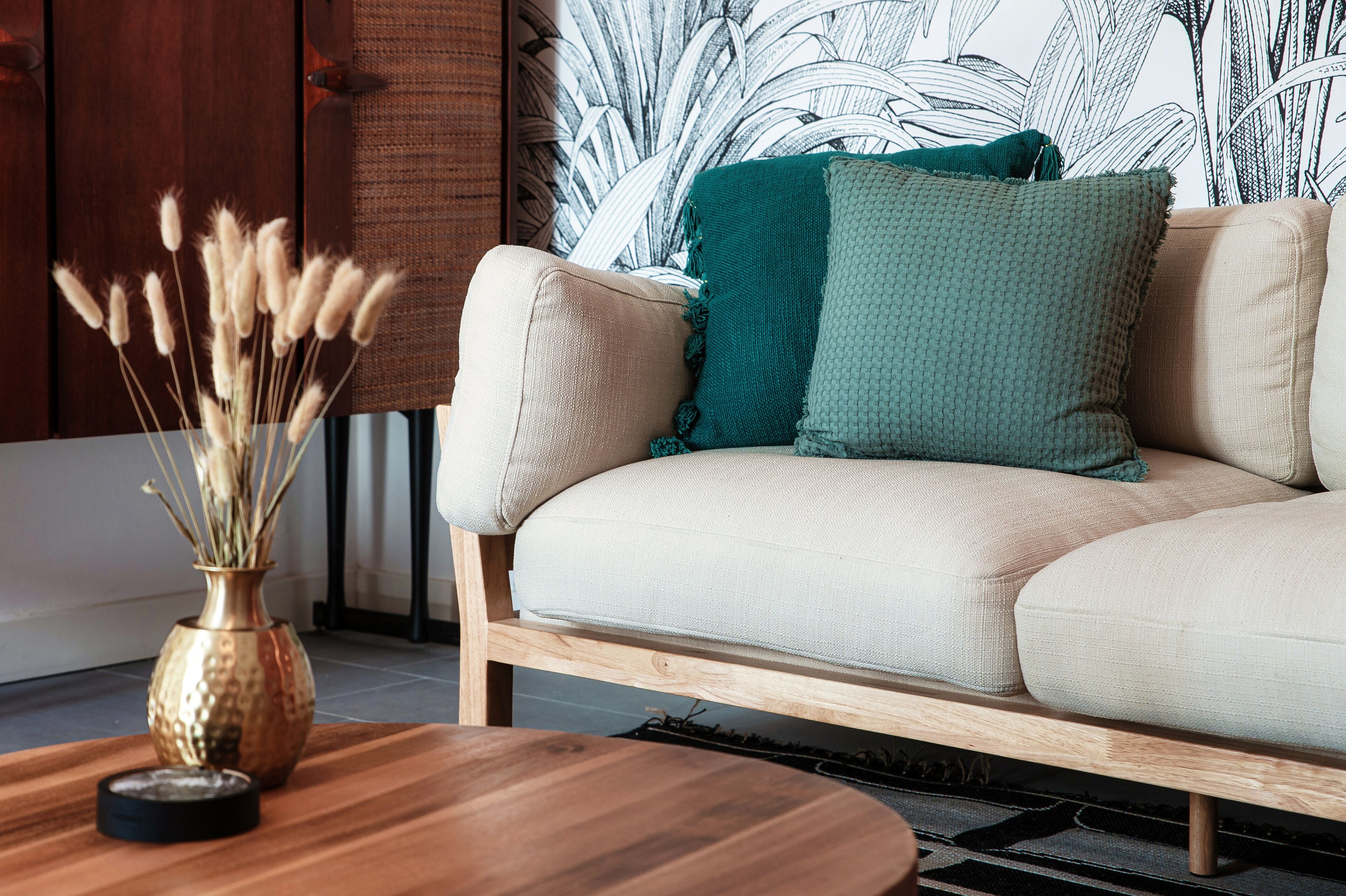 Ein Sofa mit einer gewebten Tagesdecke und einer Vase mit getrockneten Pflanzen auf einem Holztisch.