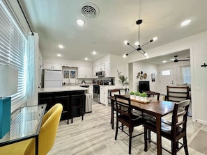 A modern kitchen with white cabinets, a central island, and a dining area with wooden chairs and a table.