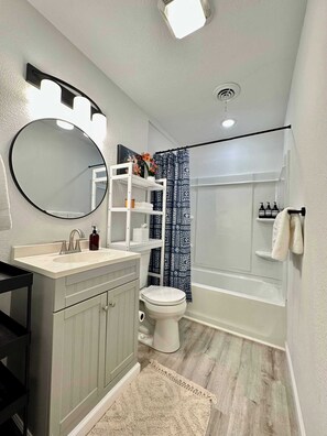 A bathroom with a toilet, sink, mirror, and shower.