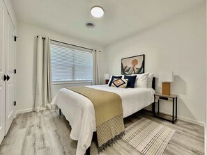 A bedroom with a bed, bedside table, lamp, and a painting on the wall.