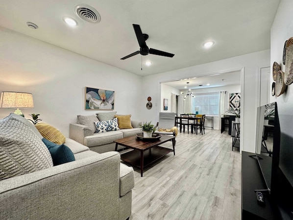 A living room with a sofa, coffee table, and TV. There is a dining area with a table and chairs.