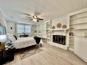 A bedroom with a bed, a ceiling fan, a fireplace, and built-in shelving.