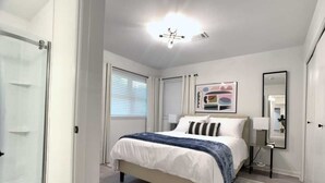 Quarto com cama, mesa de cabeceira, luminária e um espelho grande.