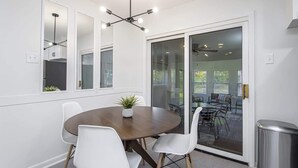 Uma sala de jantar moderna com uma mesa redonda, cadeiras brancas e um vaso de planta.