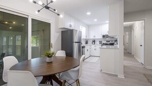 Uma cozinha moderna com armários brancos, uma ilha central e um espaço de refeições com mesa redonda e cadeiras.