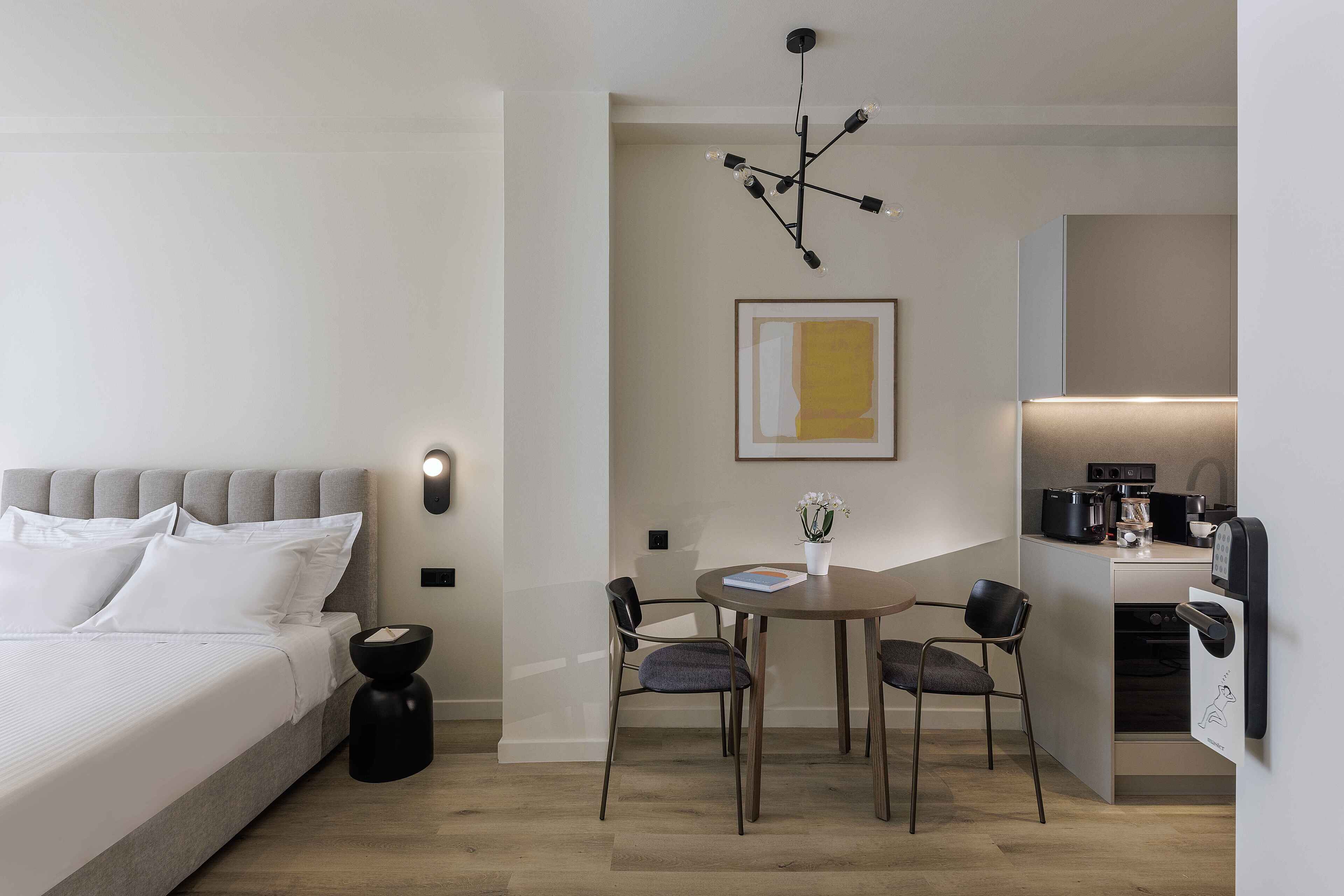 Quarto de hotel moderno com cama, mesa de cabeceira e uma pequena área de refeições com cadeiras e mesa.