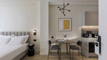 Quarto de hotel moderno com cama, mesa de cabeceira e uma pequena área de refeições com cadeiras e mesa.